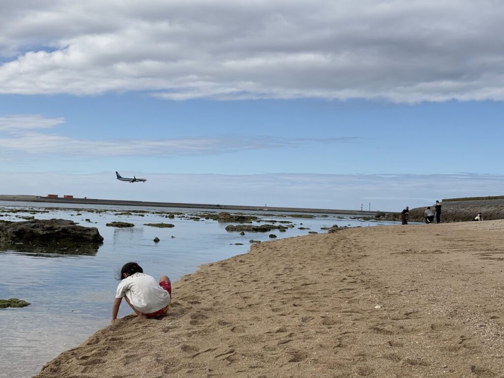 飛行機の着陸を見ながら浜辺で遊ぶ子供